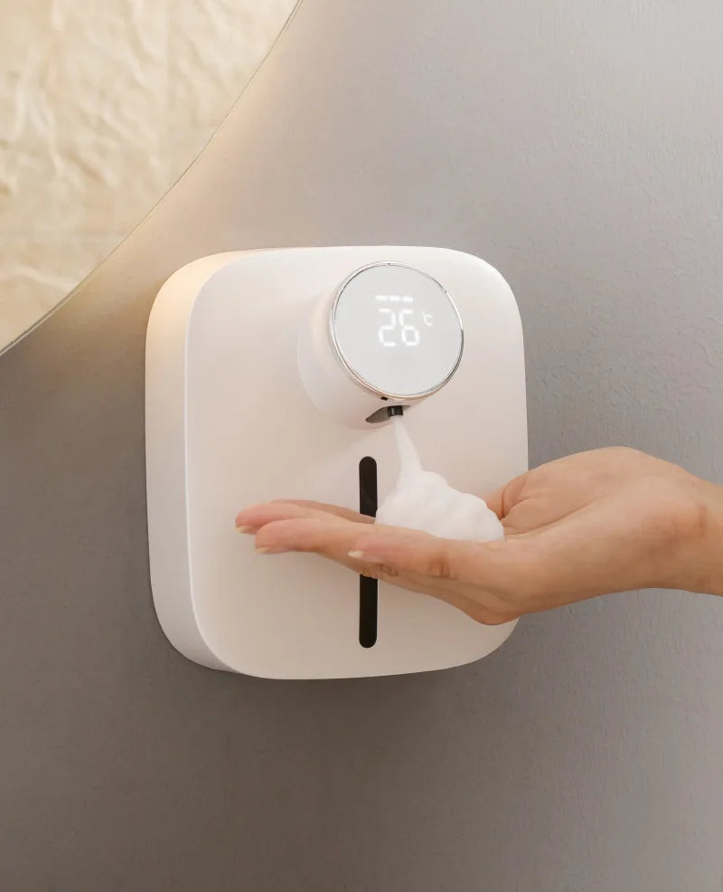 Touchless automatic soap dispenser mounted on wall, dispensing foam into a hand