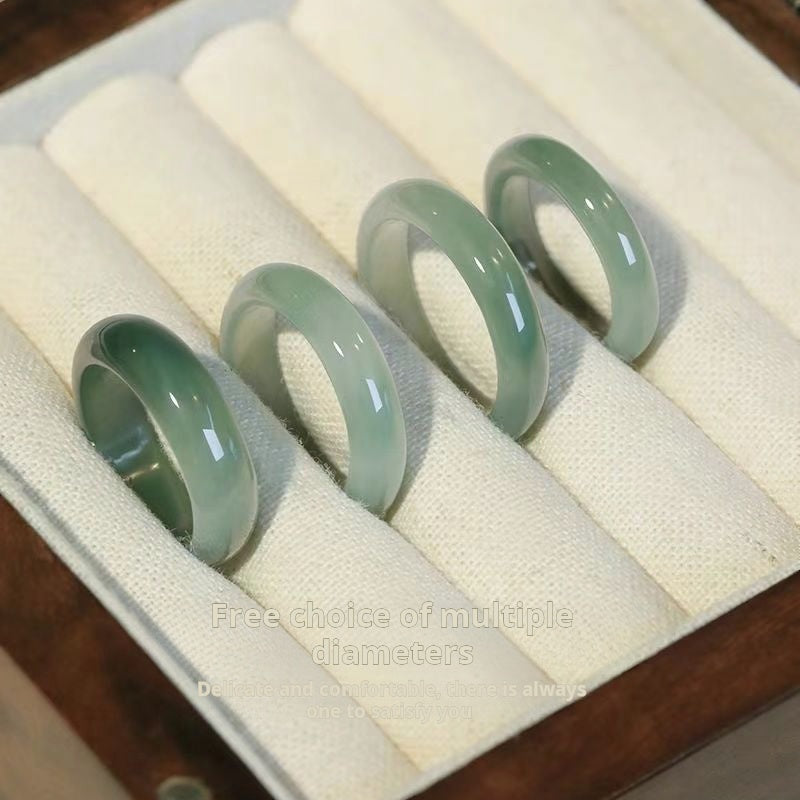Four green jade rings on a white cushion in a jewelry box.